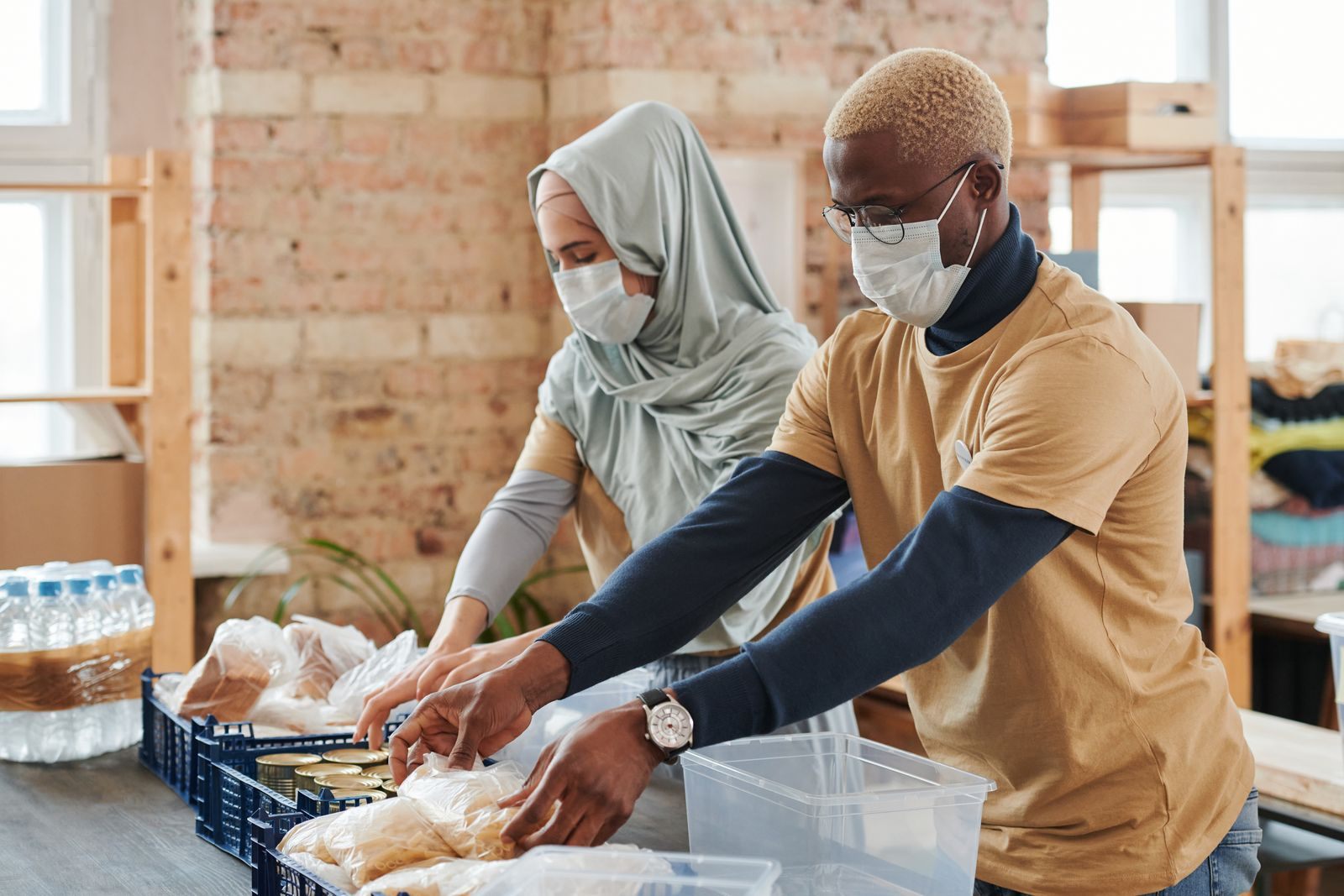 Two masked volunteers sorting and preparing food donations indoors